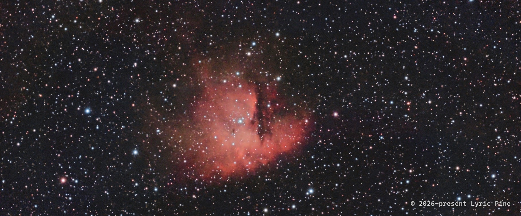 The Pacman Nebula (NGC 281): red emission clouds divided by dark dust lanes amid a dense field of stars.